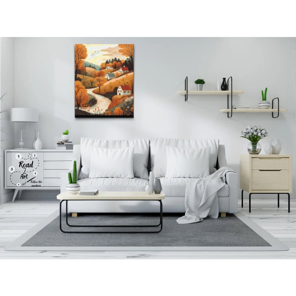 Diamond painting af et efterårslandskab med huse, træer og snoet sti i varme orange toner